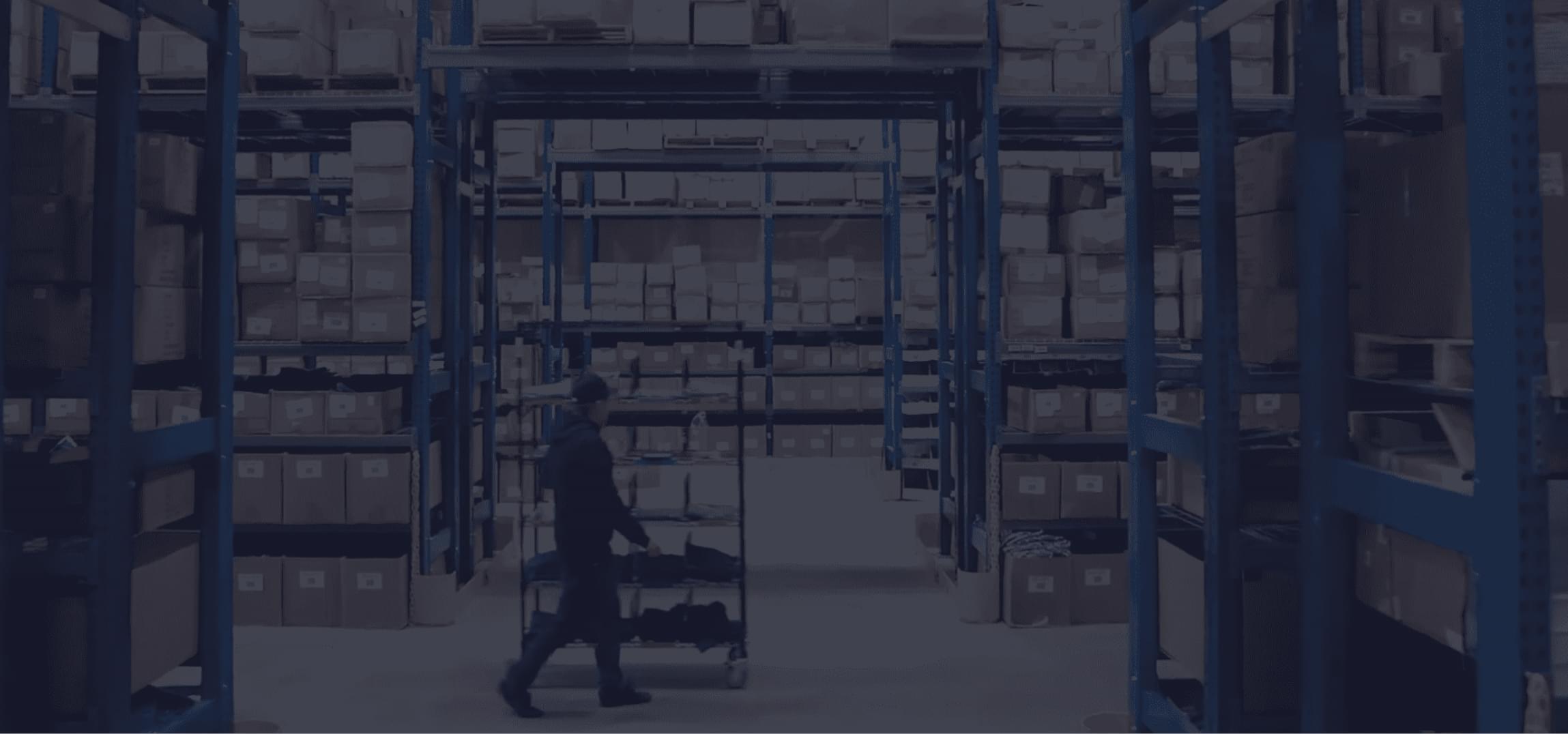 Man walking in warehouse aisle with shelves of boxes, eCommerce order fulfillment center