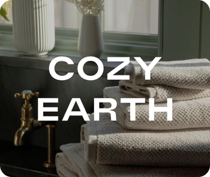 Gray cotton bath towels stacked on dark wood with brass faucet and "COZY EARTH" text overlay