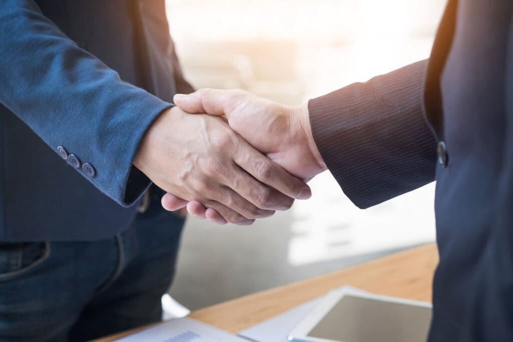 Two businessmen shaking hands over a desk, signifying a business agreement or partnership