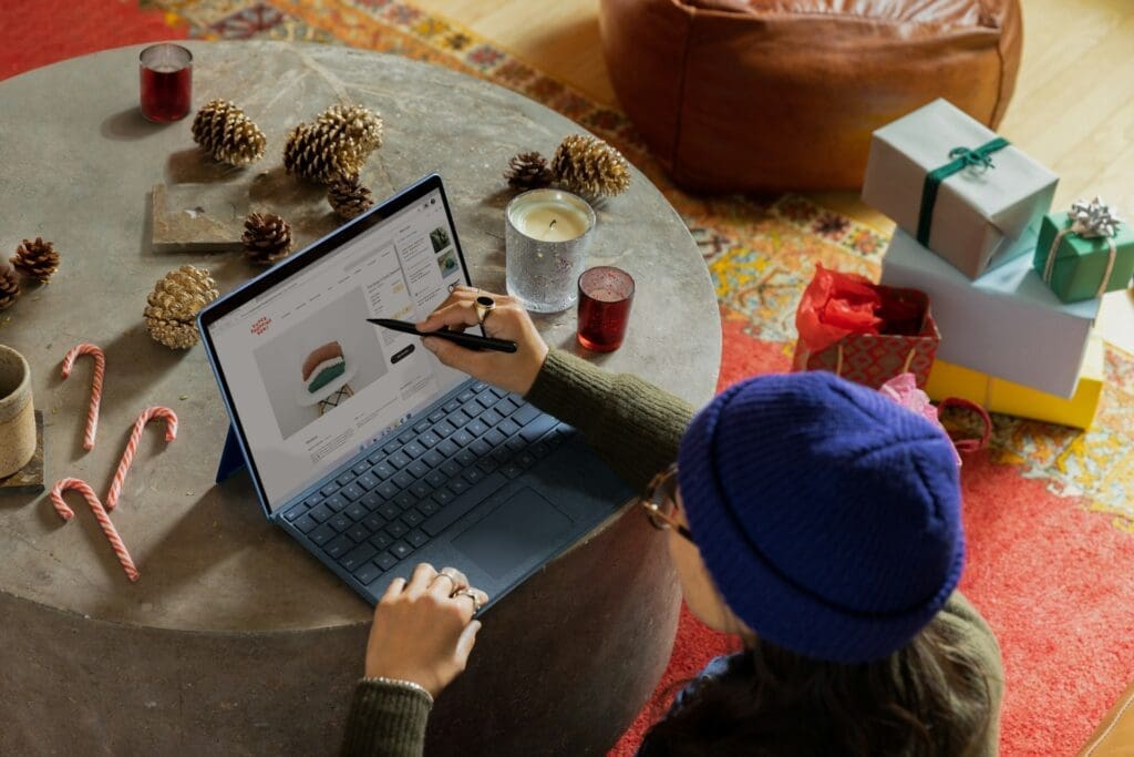 Woman ordering gifts online while sitting at table with holiday decorations and laptop computer
