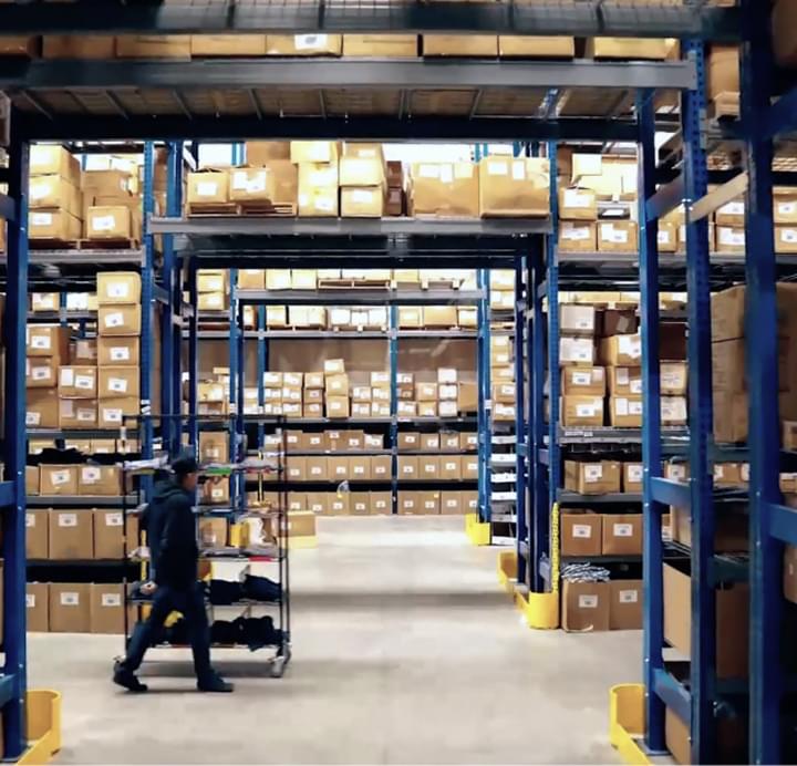 Warehouse worker pushing cart through aisles stocked with boxes for eCommerce order fulfillment
