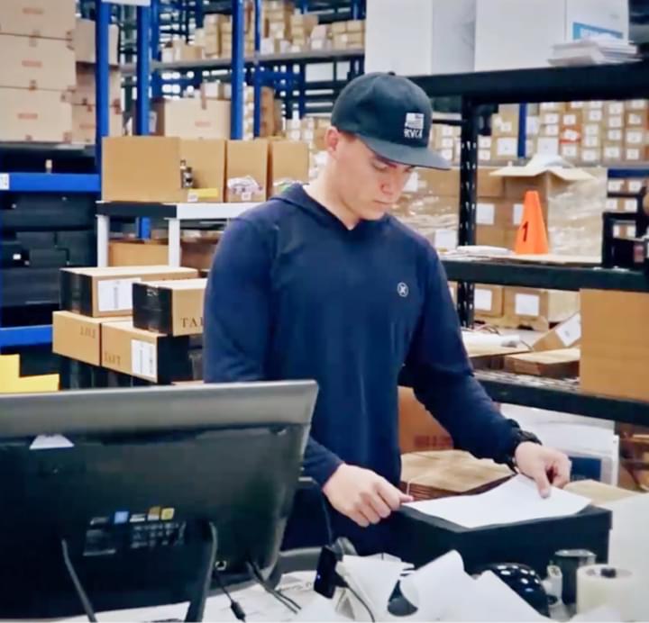 Worker in warehouse fulfillment center packing orders at computer terminal surrounded by packages