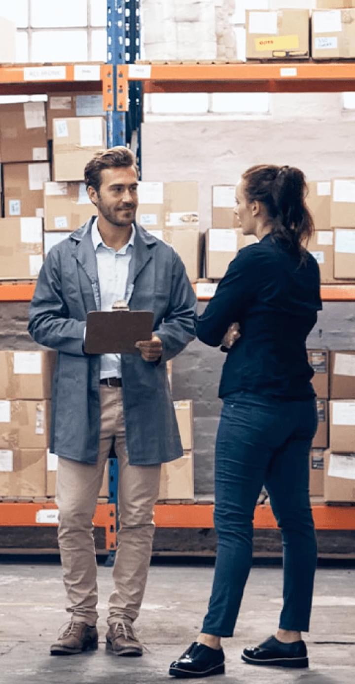 Male and female workers discussing inventory in warehouse with shelves of boxes in background