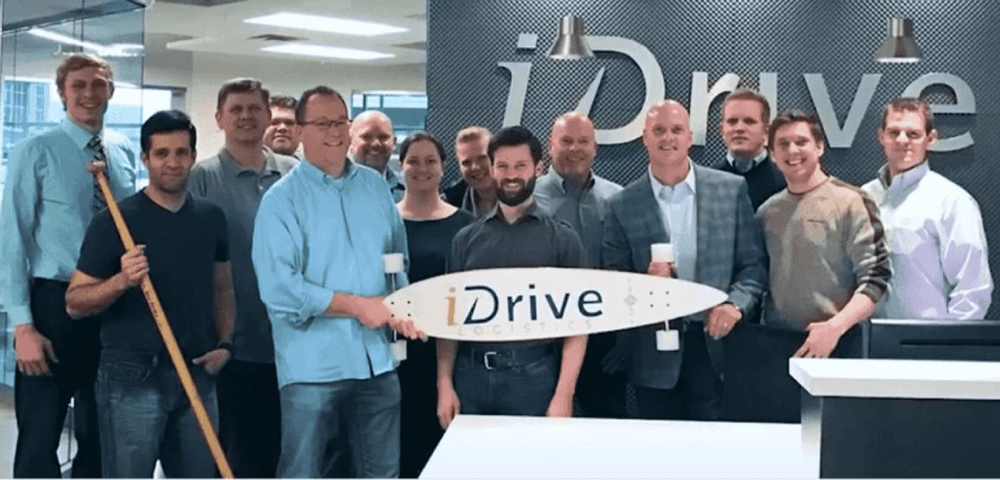 iDrive Logistics team members holding company logo sign in office