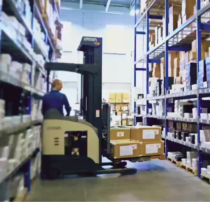 Worker operating forklift in warehouse aisle stocked with shelves of inventory boxes for eCommerce order fulfillment