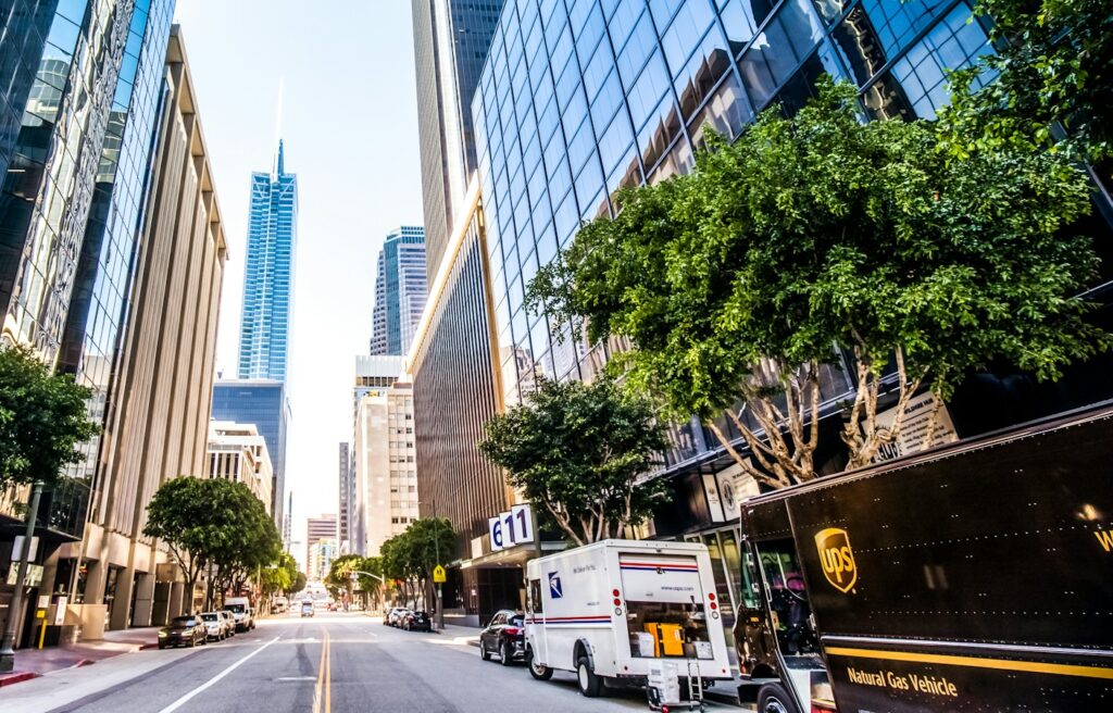 A UPS and USPS truck side-by-side in front of tall buildings